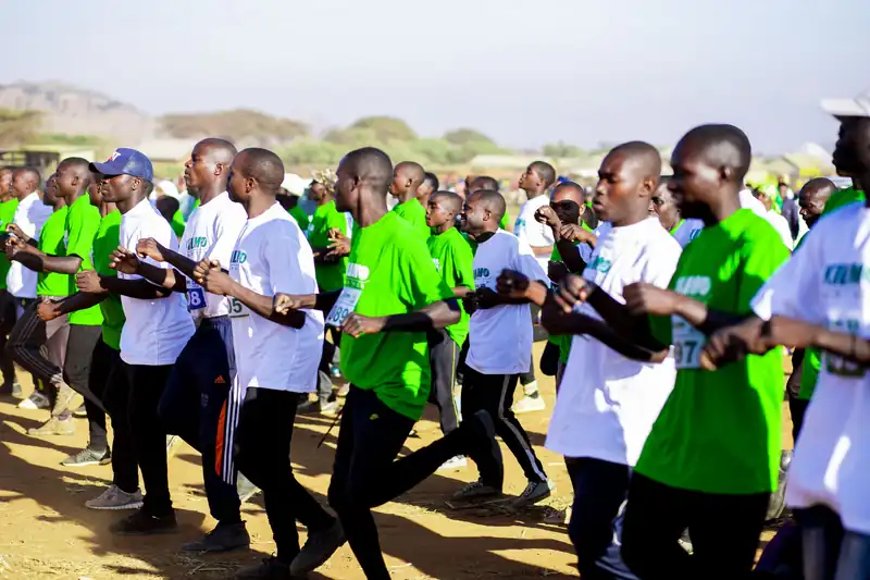 A crowd of young runners in green and white shirts setting off together