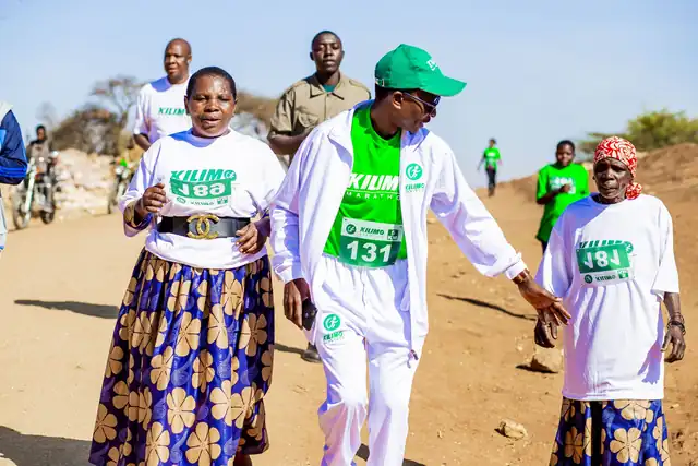 Akina mama waliovaa vitenge wakikimbia pamoja na mshiriki aliyevaa nyeupe